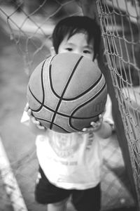 High angle portrait of boy holding ball while standing by net