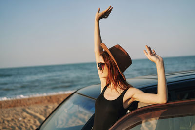 Woman with arms raised at beach against sky