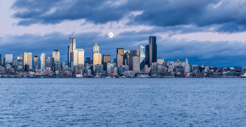 A full moon shines above the seattle skyline.