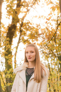Portrait of young beautiful woman standing against autumn trees