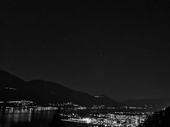 Illuminated city by sea against sky at night