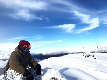 Hiker sitting on snow covered mountain against sky