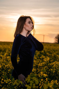 Beautiful woman standing on field against sky during sunset