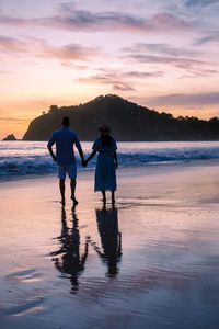 Rear view of man standing at beach against sky during sunset