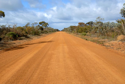 Dirt road amidst sand dunes against sky