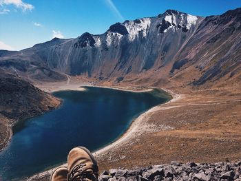 Low section of man on mountain by lake against sky