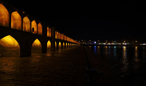 Illuminated bridge over river in city against sky at night