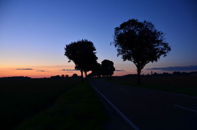 Silhouette trees on road against sky at sunset