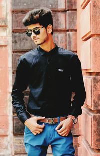 Young man wearing sunglasses standing against brick wall