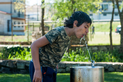 Side view of boy drinking water through fountain in park