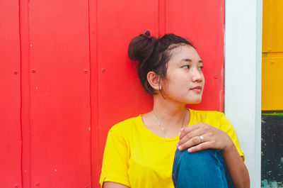 Young woman looking away while standing against door