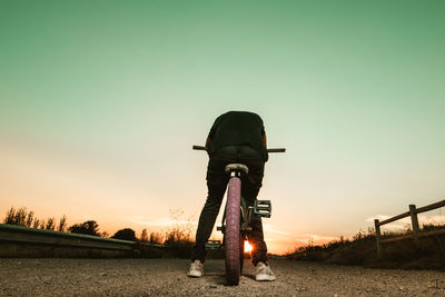 Man sitting on bicycle against sky during sunset