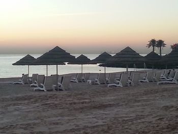 Deck chairs on beach against sky during sunset