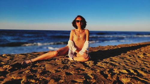 Full length of woman sitting at beach against clear sky
