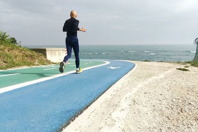 Full length of man skateboarding on sea shore against sky