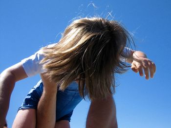 Cropped hands of father holding daughter against clear sky