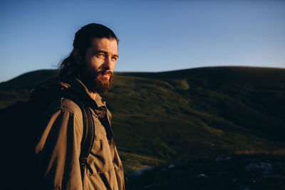 Handsome bearded man standing by mountain against clear sky