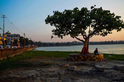 People sitting on bench by river against sky