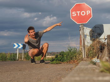 Portrait of man showing stop sign while screaming on road against cloudy sky