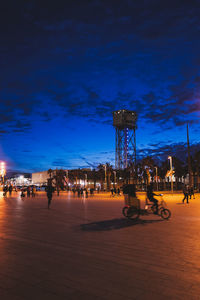 People on illuminated street lights against sky at night