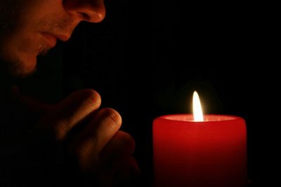 Cropped image of hand holding lit candle in dark room