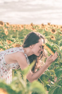 Woman by sunflower plants against sky 