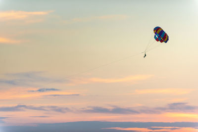 Low angle view of person paragliding against sky during sunset