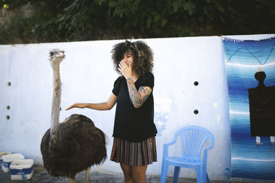 Smiling woman with ostrich standing against wall