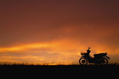 Motor scooter on grassy field against sky during sunset