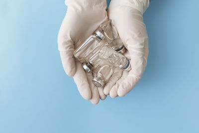 Doctor hands in gloves holding bottles of vaccine, antibiotic, other medicaments on blue background