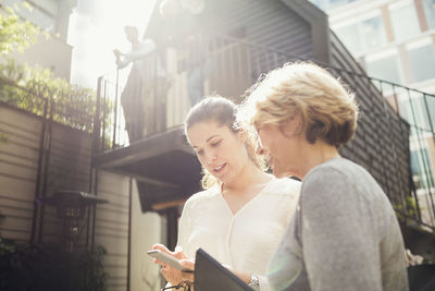 Businesswomen using mobile phone while male colleagues standing on log cabin in background