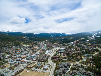 Aerial view of city at mountains against cloudy sky