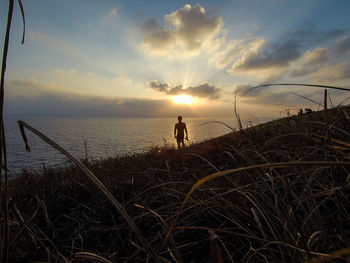 Man standing by sea against sky during sunset