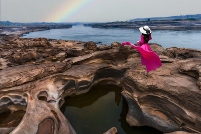 Rear view of woman sitting on rock at beach