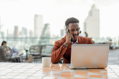 Businessman talking on phone while using laptop in cafe