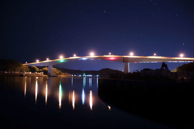 Illuminated bridge over lake against sky at night