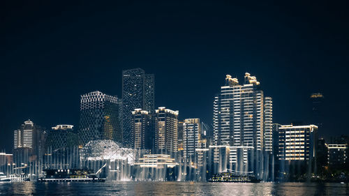 Illuminated buildings by river against sky in city at night