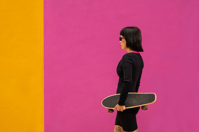 Beautiful woman with short hair posing with a skateboard on a colored background