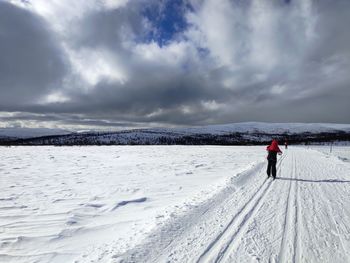 Rear view of person skiing on snow covered land against cloudy sky