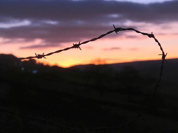 Close-up of barbed wire against sky during sunset