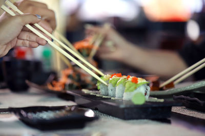 Close-up of woman hands holding sushi with chopsticks on table