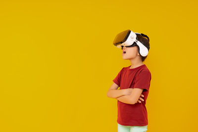 Boy wearing vr box standing against yellow background