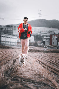 Young man running on field against sky, and following dog.