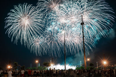 Rear view of people enjoying firework display at night