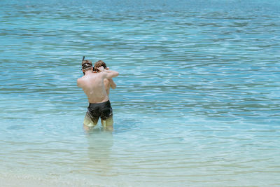 Rear view of shirtless friends standing in sea