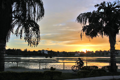 Silhouette bicycle by river against sky during sunset