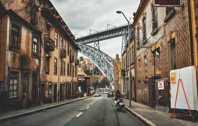 Road amidst building by metal bridge