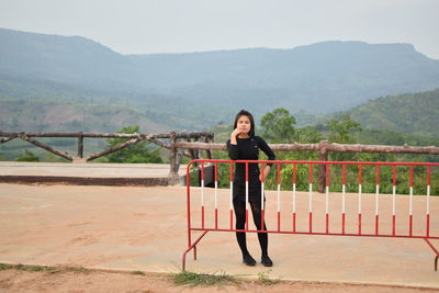 Full length portrait of woman standing by railing against mountains