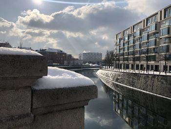 Buildings by river against sky in city during winter