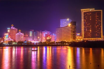 Illuminated buildings by river against sky at night